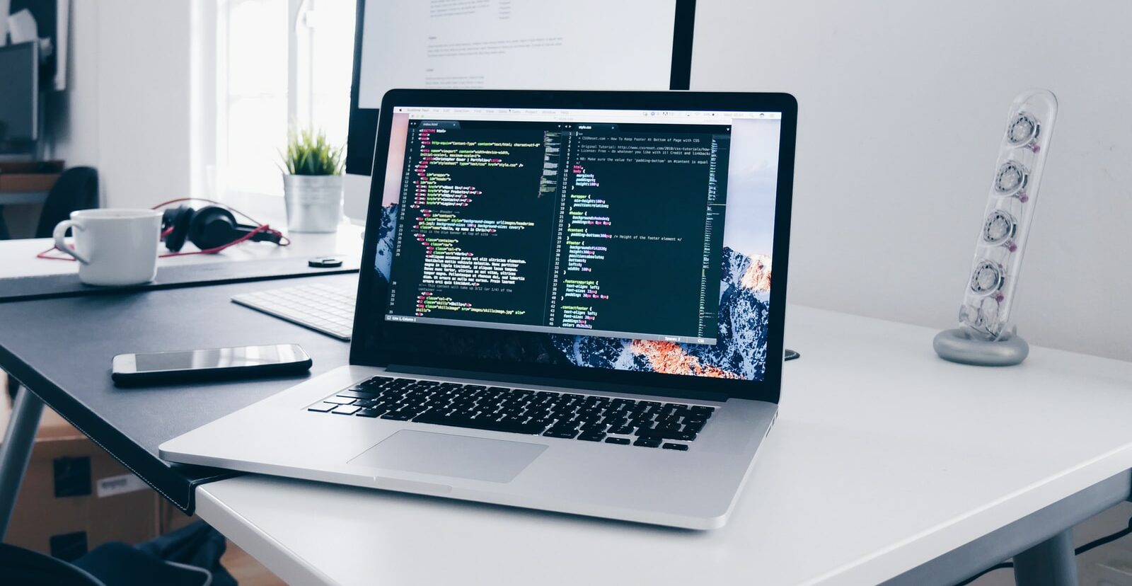 A MacBook with lines of code on its screen on a busy desk